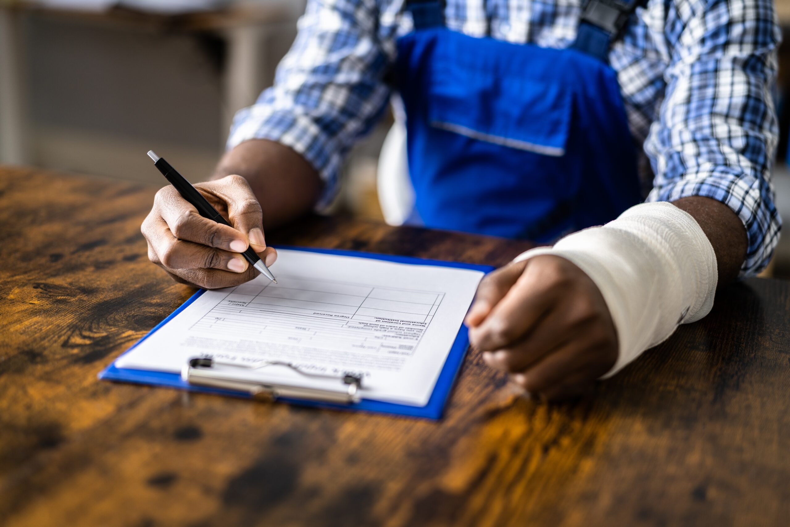 A person in a blue shirt with a bandaged hand fills out a form on a clipboard