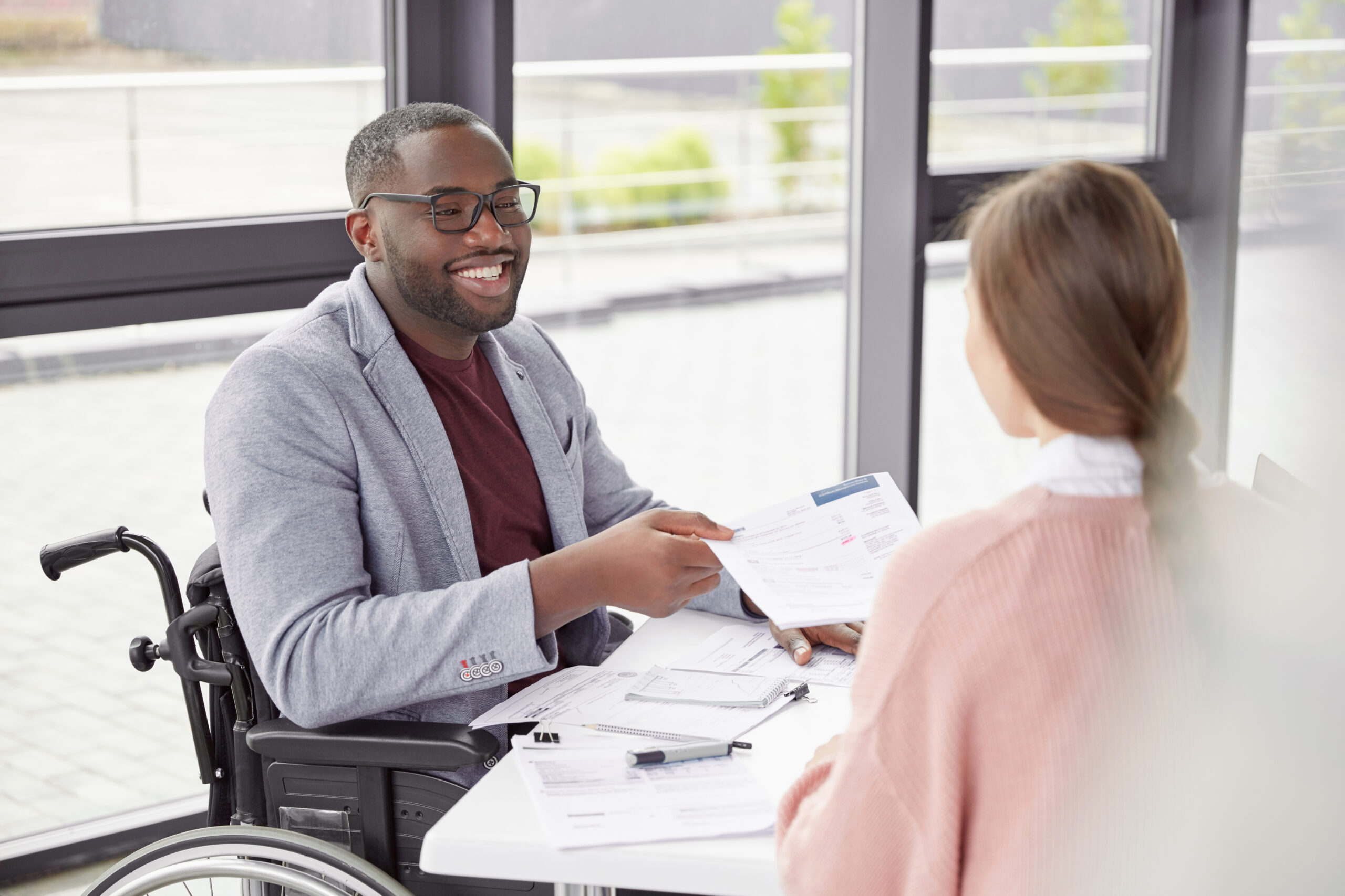 A smiling man in a wheelchair hands documents to a woman during a meeting